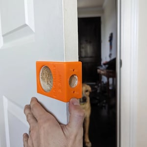 May include: Orange plastic door stop with the text "Door Stop" printed on it. The door stop is being used to hold a white door open.