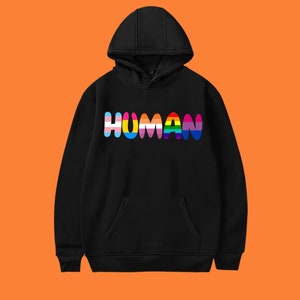 Może przedstawiać: Czarna bluza z kapturem z nadrukiem słowa "HUMAN" w kolorach tęczy z przodu.