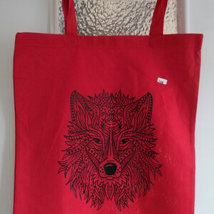 Könnte beinhalten: Rote Stofftasche mit einem schwarzen und weißen Wolf-Design. Das Gesicht des Wolfes ist mit komplizierten Mustern verziert.
