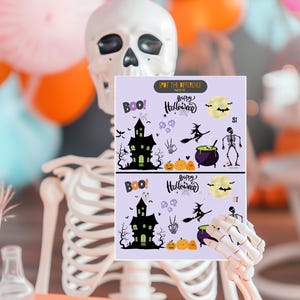 Puede incluir: Un esqueleto sostiene dos tarjetas con temática de Halloween. Las tarjetas tienen un fondo morado y presentan una casa encantada, una bruja en una escoba, un caldero, un esqueleto, murciélagos, calabazas y el texto "Feliz Halloween" y "¡Boo!"