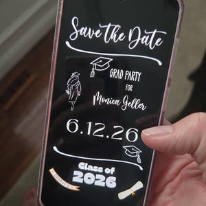 May include: A smartphone displays a graduation announcement. The black screen features white script reading "Save the Date" and "Grad Party for Monica Geller 6.12.26 Class of 2026." Decorative graduation cap and scroll icons are also present.