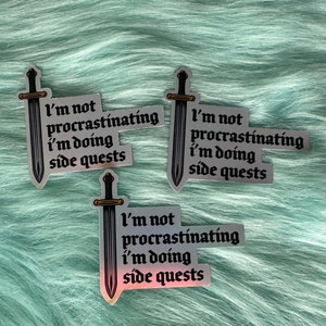 Puede incluir: Tres pegatinas hologr&aacute;ficas con el texto "I'm not procrastinating, I'm doing side quests" y una ilustraci&oacute;n de espada. Las pegatinas tienen un acabado met&aacute;lico plateado y est&aacute;n sobre un fondo azul claro y suave.