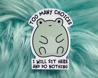 May include: A die-cut sticker featuring a round, light green cartoon frog with pink cheeks and a neutral expression. The text above reads TOO MANY CHOICES and the text below reads I WILL SIT HERE AND DO NOTHING in bold black capital letters.