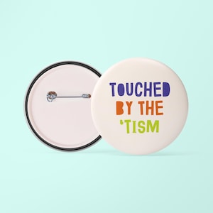 May include: White button with blue, orange and green text that reads "TOUCHED BY THE 'TISM". The back of the button is blank with a pin.