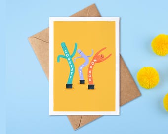 Op de afbeelding: Een rechthoekige wenskaart met een gele achtergrond en drie kleurrijke opblaasbare buisfiguren. Het groenblauwe figuur toont CONGRATS, het paarse figuur YAY en het oranje figuur WOO HOO in witte letters.