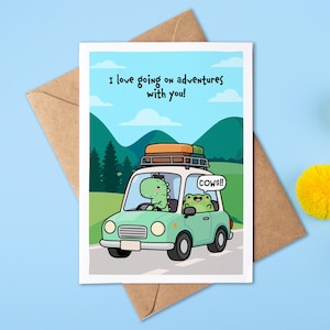 May include: A greeting card featuring a light green car with a roof rack, driven by a green dinosaur with a frog passenger. The text reads, I love going on adventures with you! and the frog says, COWS!!. The background shows mountains and sky.