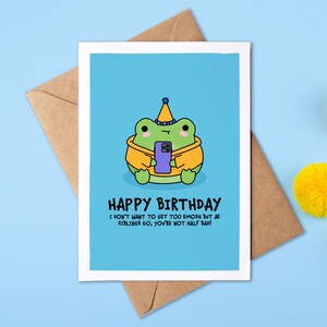 May include: A birthday card featuring a cartoon frog in a party hat, holding a phone. The card reads "HAPPY BIRTHDAY" and a message for a sibling. The card is on a blue surface with yellow pom-poms and a brown envelope.