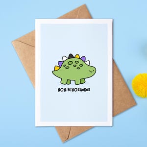 May include: A greeting card featuring a cartoon green dinosaur with a purple, yellow, black and white striped back. The text on the card reads "NON-BINOsaurus".