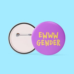 May include: A purple badge with the words "EWWW GENDER" in yellow, next to a badge back with a pin. The badges are on a light blue background. The badge is a round shape.