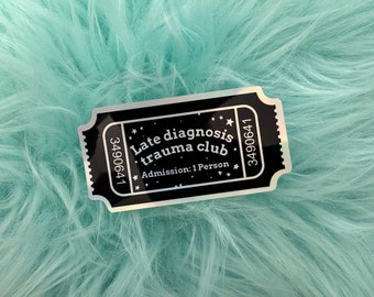 May include: A black ticket-shaped sticker with the text "Late diagnosis trauma club" and "Admission: 1 Person". The sticker has a silver border and is set against a fluffy, light blue background.