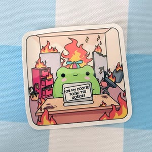 May include: A square sticker featuring a green frog wearing a propeller hat, sitting at a desk with a laptop that reads ON MY POOTER DOING THE WORKIES. The office scene is engulfed in orange and yellow flames, including a pink filing cabinet.
