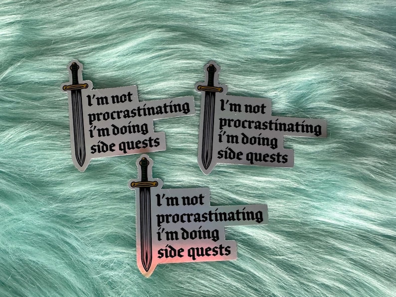 Puede incluir: Tres pegatinas hologr&aacute;ficas con el texto "I'm not procrastinating, I'm doing side quests" y una ilustraci&oacute;n de espada. Las pegatinas tienen un acabado met&aacute;lico plateado y est&aacute;n sobre un fondo azul claro y suave.