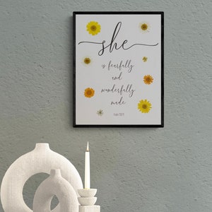 May include: A framed print with a white background and black frame. The print features a floral design with yellow and white flowers and the text "she is fearfully and wonderfully made Psalm 139:14".