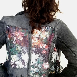 Può includere: Una giacca di jeans nera con un pannello posteriore in pizzo floreale. La giacca ha un orlo sfrangiato ed è corta.