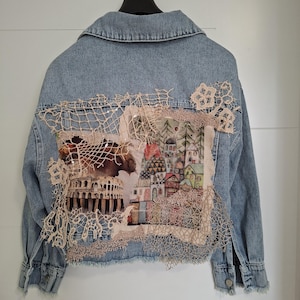 Può includere: Giacca di jeans azzurra con un pannello posteriore decorativo con un'illustrazione ad acquerello di un paesaggio urbano europeo e del Colosseo, impreziosita da pizzo beige. La giacca ha un colletto classico e polsini abbottonati.