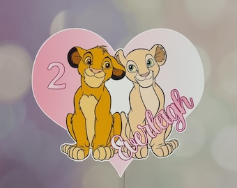 May include: A pink heart-shaped cake topper featuring a cartoon image of Simba and Nala from The Lion King. The topper reads "2 Everleigh" in pink lettering.