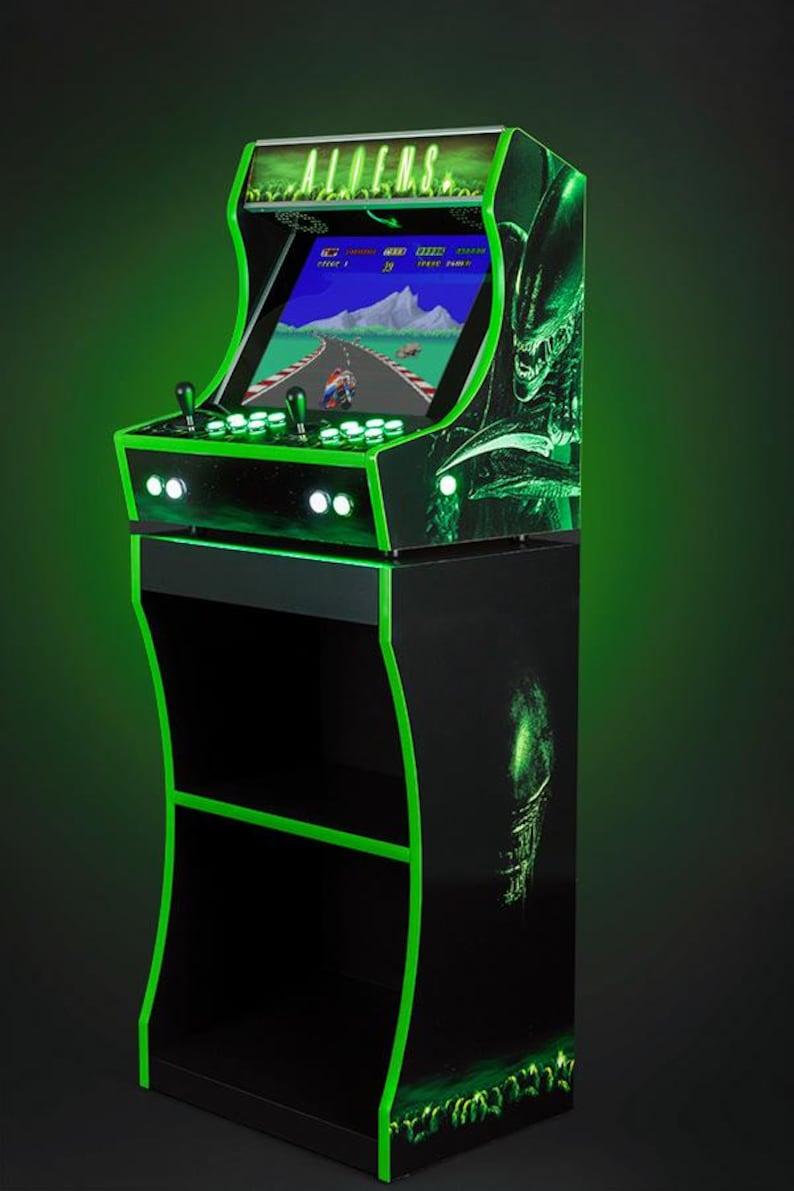 May include: A black and green arcade cabinet with a green neon outline. The cabinet has a screen displaying a video game with the text "ALIENS" on the top. The cabinet has a stand with two shelves.