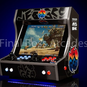 May include: A black arcade cabinet with a colourful Neo Geo logo. The cabinet has a screen displaying a video game with a desert background. The screen shows the text "CREDITS 20" and "R72". The cabinet also has a Neo Geo MVS SNK logo.