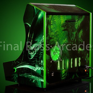 May include: A green arcade cabinet featuring a black and green alien graphic. The cabinet has a green light and the text "ALIENS" on the front.