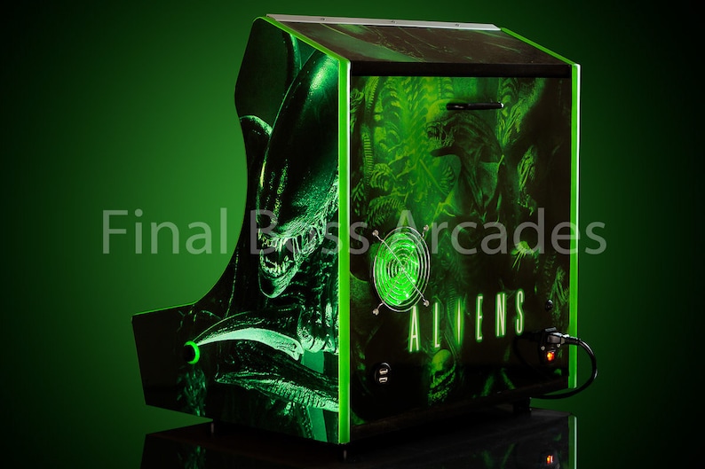 May include: A green arcade cabinet featuring a black and green alien graphic. The cabinet has a green light and the text "ALIENS" on the front.