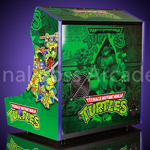 May include: A green and purple arcade cabinet featuring a Teenage Mutant Ninja Turtles theme. The cabinet has a comic book style design with images of the four turtles. The text "TEENAGE MUTANT NINJA TURTLES" is printed on the cabinet.