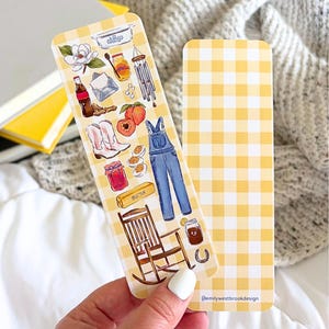 May include: Two decorative bookmarks. One features a yellow gingham pattern. The other has a yellow gingham background with illustrations of a rocking chair, overalls, boots, peaches, and other country-themed images.