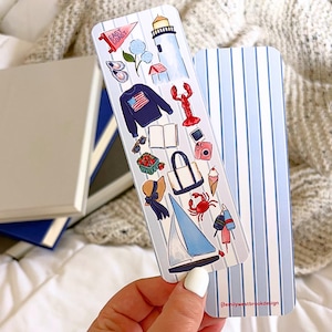 May include: A blue and white striped bookmark with nautical-themed illustrations. The bookmark features drawings of a lighthouse, lobster, sailboat, and other coastal elements. The text "EAST COAST" is visible on a pennant.