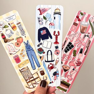 May include: Three decorative bookmarks with watercolor illustrations. One features a yellow gingham pattern with peaches, boots, and overalls. Another has a striped pattern with a lighthouse, lobster, and sweater. The third has a pink striped pattern with cherries and sunglasses.
