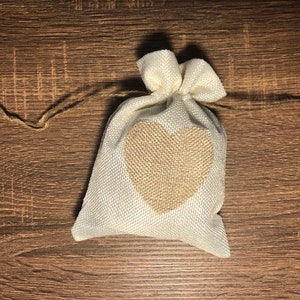 May include: A small white burlap bag with a brown heart design. The bag is tied with a brown twine string.