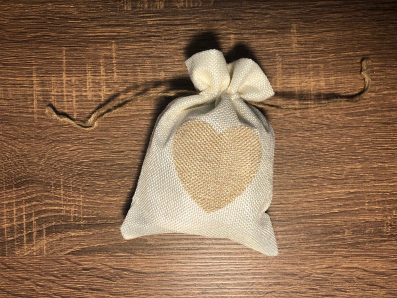May include: A small white burlap bag with a brown heart design. The bag is tied with a brown twine string.