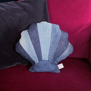 Könnte beinhalten: Ein Kissen in Form einer Muschel aus Jeansstoff auf einem rosa und grauen Hintergrund. Das Kissen liegt auf einem Sofa mit einem rosa und grauen Hintergrund.