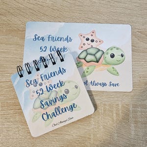 May include: A spiral-bound savings challenge notebook and a matching card featuring a sea turtle and starfish design. The notebook and card have the text "Sea Friends 52 Week Savings Challenge" and "Ond Always Save" in a whimsical font.