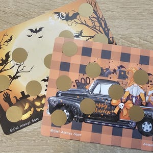 May include: Two Halloween scratch-off cards. One card shows bats, a full moon, and a pumpkin. The other card has a black truck with gnomes and the text "Happy Halloween". Both cards have gold scratch-off circles.