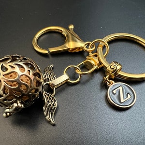 May include: Gold-tone keychain with a round, openwork charm with a brown center. The charm is attached to a gold-tone split ring and a gold-tone chain with a small, round charm with the letter "Z" on it.