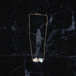 May include: A gold chain necklace with a pendant made of several small, white, and beige stones. The necklace is on a black background.