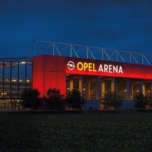 May include: An exterior view of a large red stadium with the words "Opel Arena" in yellow letters on the front.