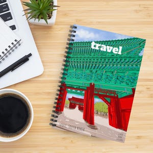May include: A spiral-bound notebook featuring a colorful illustration of a traditional Korean gate structure with vibrant green roof tiles and bright red pillars. The word travel is printed in white at the top, with Seoul, South Korea below.