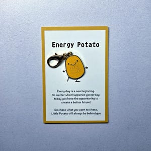 May include: A yellow card with the text "Energy Potato" and a charm shaped like a smiling potato. The card also includes inspirational text. The charm has a lobster clasp.