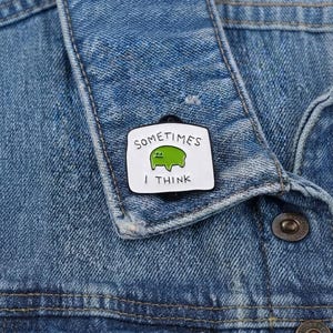 May include: A rectangular enamel pin with a white background and a black border. The pin features a small green blob-like character in the centre with the text "SOMETIMES" above it and "I THINK" below it in black, sans-serif capital letters.