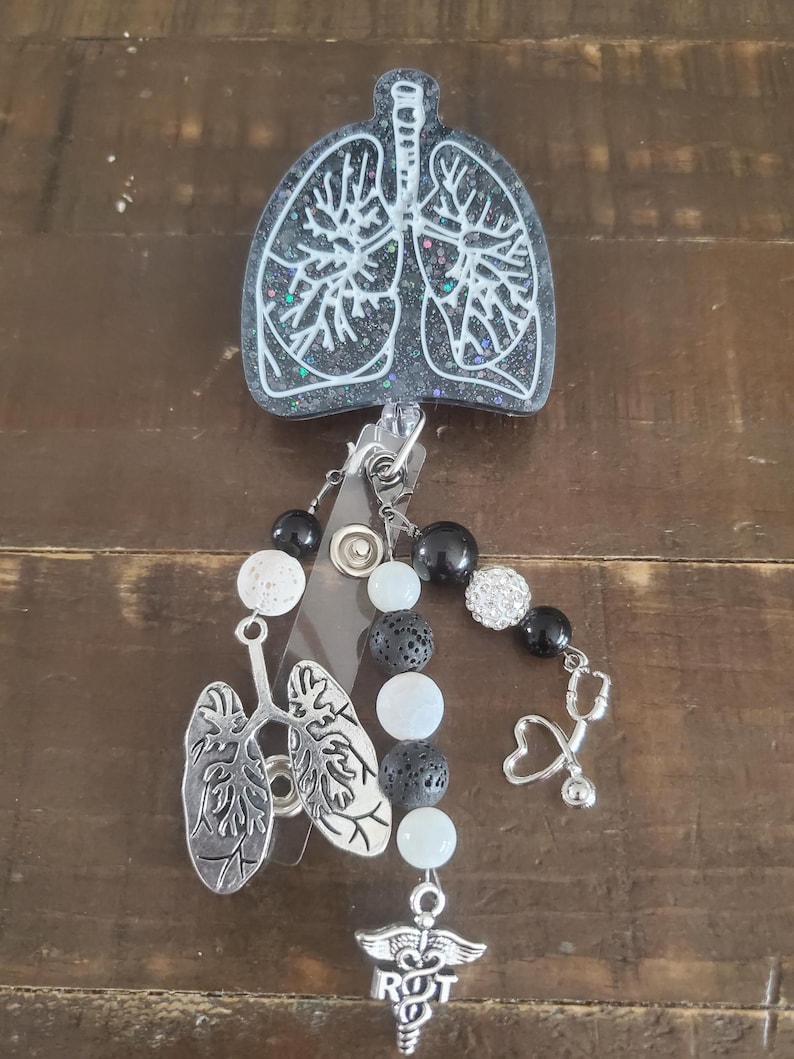 May include: Black and white resin badge reel with a white outline of lungs, black lava rock beads, white beads, a silver charm of lungs, a silver stethoscope charm, and a silver charm with a caduceus and the letters RRT.