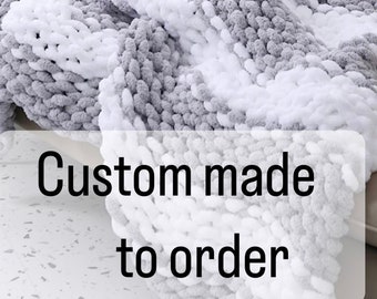 May include: A gray and white chunky knit throw blanket with a custom made to order label. The blanket is made of soft yarn and has a textured look.