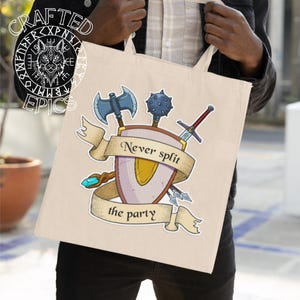 Könnte beinhalten: Beige Tragetasche mit einem Schilddesign und dem Text "Never split the party". Das Design umfasst eine blaue Axt, eine Keule, ein Schwert und andere Fantasy-Waffen. Die Tasche hat ein "Crafted Epics"-Logo.