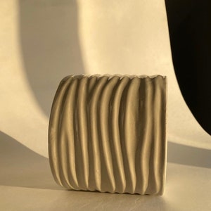May include: A grey ceramic planter with a wavy, textured design. The planter is empty and sitting on a white surface.