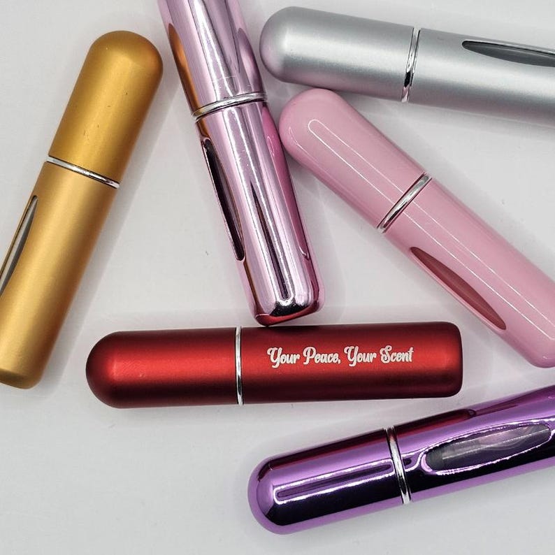 May include: An assortment of refillable perfume atomizers in various colors, including gold, pink, silver, and red. The red atomizer has the text "Your Peace, Your Scent" printed on it. Each atomizer has a metallic finish and a silver band.