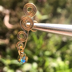 May include: Gold ear cuff with a dangling iridescent crystal. The ear cuff is made of wire that is twisted into a spiral shape.