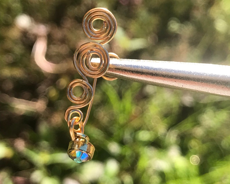 May include: Gold ear cuff with a dangling iridescent crystal. The ear cuff is made of wire that is twisted into a spiral shape.