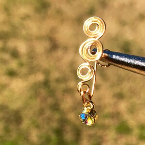 May include: Gold wire ear cuff with a dangling iridescent crystal. The ear cuff is made of multiple intertwined circles.