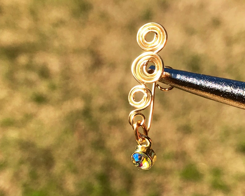 May include: Gold wire ear cuff with a dangling iridescent crystal. The ear cuff is made of multiple intertwined circles.