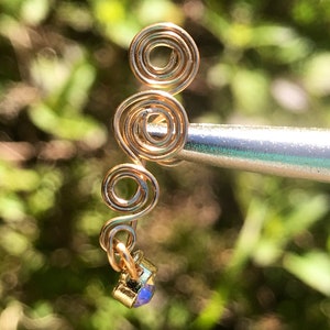 May include: Gold wire ear cuff with a spiral design and a small iridescent gemstone at the bottom.