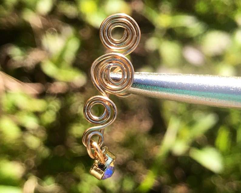 May include: Gold wire ear cuff with a spiral design and a small iridescent gemstone at the bottom.